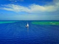 Aerial photo of a sailboat navigating through a tropical pass between reefs