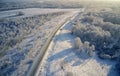 Aerial photo of winter road surrounded by birch forest. Drone shot of trees covered with hoarfrost and snow