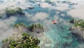 Aerial of red airplane flying over coastal landscape with rocks and trees.