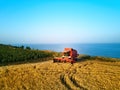 Aerial of red combine harvester working in wheat field near cliff with sea view on sunset. Harvesting machine cutting Royalty Free Stock Photo