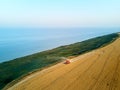 Aerial of red combine harvester working in wheat field near cliff with sea view on sunset. Harvesting machine cutting