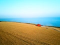 Aerial of red combine harvester working in wheat field near cliff with sea view on sunset. Harvesting machine cutting