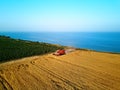 Aerial of red combine harvester working in wheat field near cliff with sea view on sunset. Harvesting machine cutting Royalty Free Stock Photo