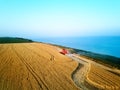 Aerial of red combine harvester working in wheat field near cliff with sea view on sunset. Harvesting machine cutting Royalty Free Stock Photo