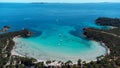 Aerial of Rondinara's populated beach with ships in the sea and trees on the sand