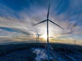 Aerial scenic view on Sunset on round Earth, curved horizon line with windmills farm rising above winter pine tree forest,