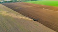 Aerial shot of agricultural field with tractor pulling a disc harrow over agricultural field, farmland