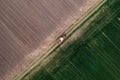 Aerial shot of agricultural tractor with crop seeder attached driving along dirt road through plowed fields, drone pov