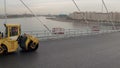 Aerial shot of alphalt compactors pressuring new asphalt paved on modern cable-stayed bridge on a background of river in