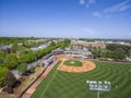 aerial shot of a baseball game with players on the fields, lush green grass and trees, people in the stands