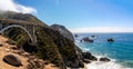 Aerial shot of the California Bixby bridge on a green hill near beautiful blue water