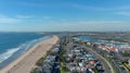 Aerial shot of the coastline with blue ocean water and homes along the sand on the beach, cars driving on the street and blue sky