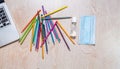 Aerial shot of colored pencils with disinfectant gel, mask and a laptop detail Royalty Free Stock Photo