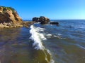 An aerial shot of a gorgeous summer landscape at the beach with blue ocean water and waves crashing into the large rocks Royalty Free Stock Photo