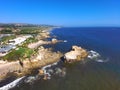 An aerial shot of a gorgeous summer landscape at the beach with blue ocean water and waves crashing into the large rocks Royalty Free Stock Photo