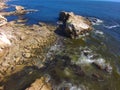 An aerial shot of a gorgeous summer landscape at the beach with blue ocean water and waves crashing into the large rocks Royalty Free Stock Photo