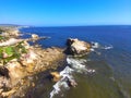 An aerial shot of a gorgeous summer landscape at the beach with blue ocean water and waves crashing into the large rocks Royalty Free Stock Photo