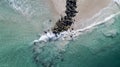 Aerial shot of the ocean waves breaking by the pile of rocks on the beach Royalty Free Stock Photo