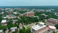 aerial shot of office buildings, dorms and apartments in city skyline surrounded by vast miles of lush green trees with blue sky