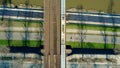 Aerial shot of passenger train moving on railway bridge across the river and bicycle road, top view. Ecologic