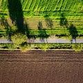 Aerial shot of a road separating a green field and a plowed one