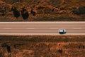 Aerial shot of single gray car driving down the road through countryside in late summer