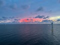 Aerial shot of windmills in the ocean and the red sky above clouds at sunset Royalty Free Stock Photo