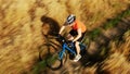 Aerial telephoto lens tracking shot of an athletic man riding fast along rye field pathway