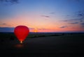 Aerial, side view of the evening landing of shining red-blue hot air balloon against sunset. Red hot air balloon firing its burner