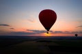 Aerial, side view of the evening landing of shining red-blue hot air balloon against sunset. Red hot air balloon firing its burner