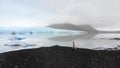 Aerial side view female person walk by Fjallsjokull glacier in overcast day in Iceland