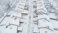 AERIAL: Silver car driving down the snowy road leading through the suburbs. Royalty Free Stock Photo