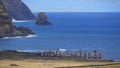 AERIAL: Tiny tourists taking photos of a line of moai statues by the ocean.