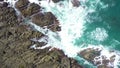 Aerial view of ocean wave crashing on rocky cliff with white spray and foam on deep blue sea water after storm