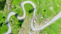 Aerial: top down view tailspin over winding mountain road on the Italian Alps, crossing green meadow and pasture in alpine valley,