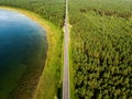 Aerial top down view of two-lane road with pine tree forests on one side, and green lake on the other. Beautiful summer scenery in Royalty Free Stock Photo