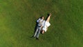 AERIAL TOP DOWN: Young happy pregnant couple lying down on grass on sunlit day Royalty Free Stock Photo