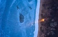 Aerial top view from above of lonesome car at frozen sea coastline with headlights on. Lonely road trip traveller enjoys