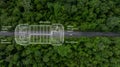 Aerial top view of green electric vehicle car driving over straight forest road, EV car electric vihicle car on forest road with