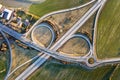 Aerial top view of modern highway road intersection, house roofs on spring green field background. Drone photography