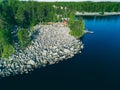 Aerial top view of red log cabin or cottage with a sauna in a green forest near a lake with rocky coast in Finland Royalty Free Stock Photo