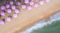 Aerial top view on the sandy beach. Pink umbrellas, sand, beach chairs and sea waves