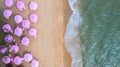 Aerial top view on the sandy beach. Pink umbrellas, sand, beach chairs and sea waves