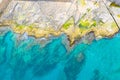 Aerial top view of sea waves hitting rocks on the rocky beach with green algae with turquoise sea water. Seascape in the coastline Royalty Free Stock Photo