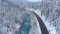 AERIAL: Tourist cars cruising through snowy woods and along a emerald river. Royalty Free Stock Photo