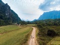 Aerial: tourist couple riding mountain bike on dirt road in scenic landscape around Vang Vieng backpacker travel destination in