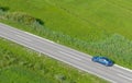 AERIAL: Tourist in a blue Tesla drives down scenic road crossing the countryside