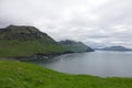 AERIAL: Towering grassy cliff facing the endless blue ocean on a cloudy day. Royalty Free Stock Photo