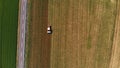 Aerial: tractor working on cultivated fields farmland, agriculture occupation, top down view of lush green cereal crops, sprintime