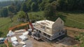 AERIAL: Truck boom lifts a massive CLT wall panel as workers assemble a house.